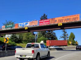 a series of multicoloured banners draped over a freeway. The banners advocate to stop the TMX pipeline, and activists on top of the bridge cheer