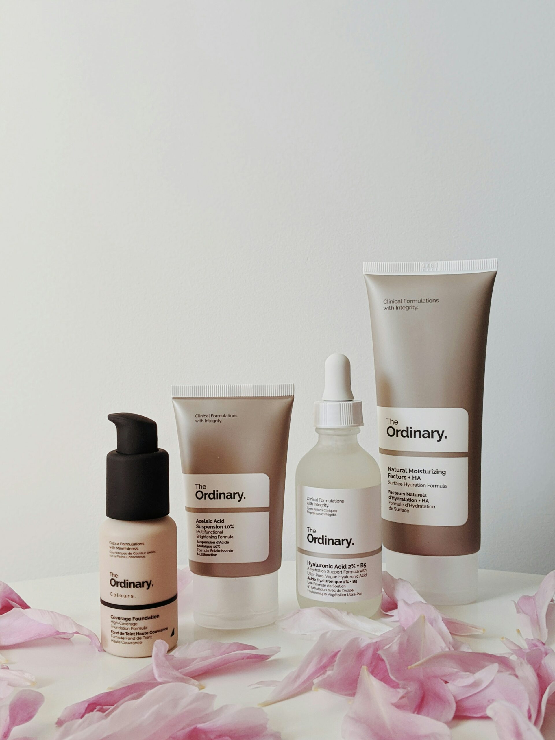 A photo of four skincare products against a white backdrop from the brand The Ordinary. The products are labeled: high coverage foundation, azelaic acid, hyaluronic acid, and natural moisturizing factors + HA.