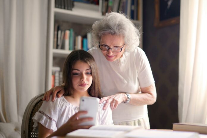 Young girl showing something on her phone to her grandmother who is standing behind her.