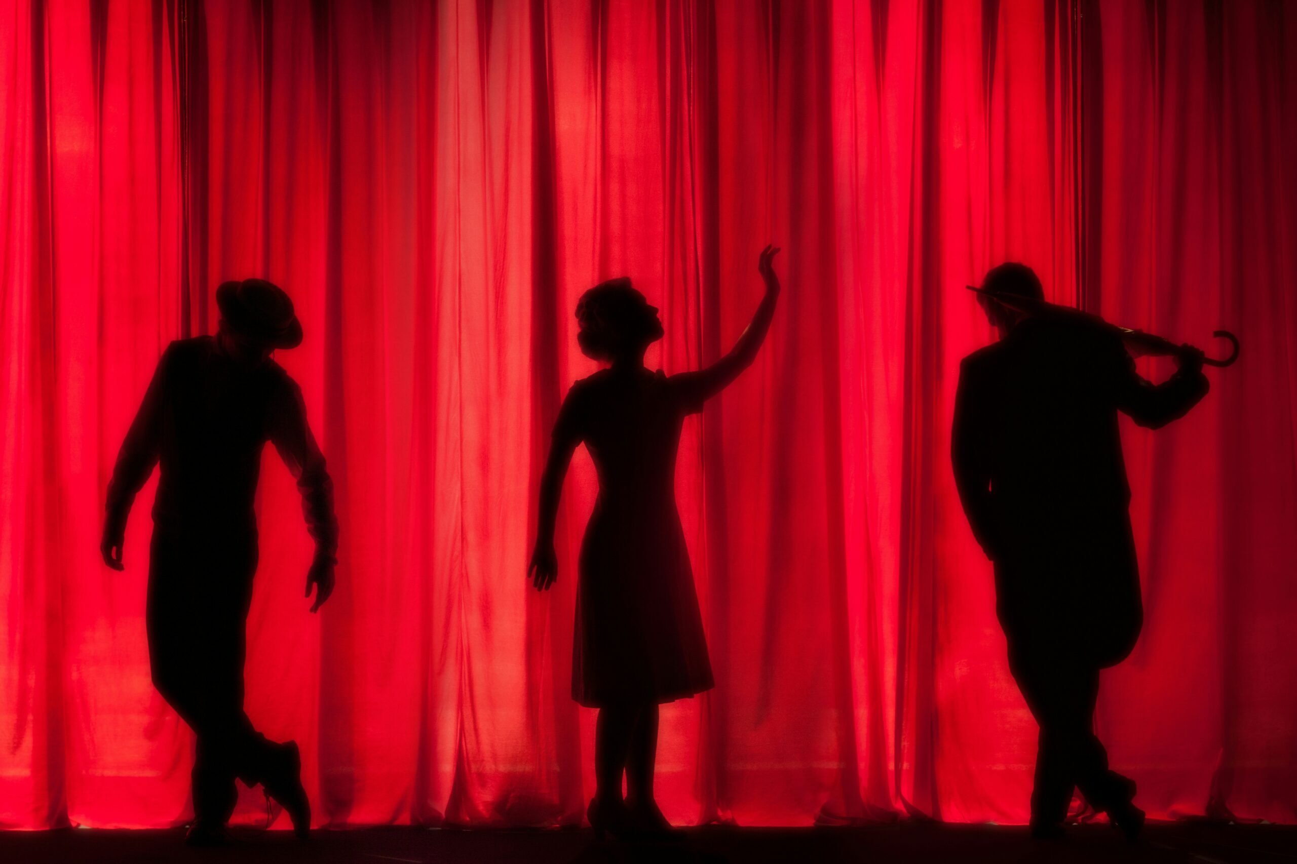 A dimly lit theatre with black silhouettes of performers against a red curtain.