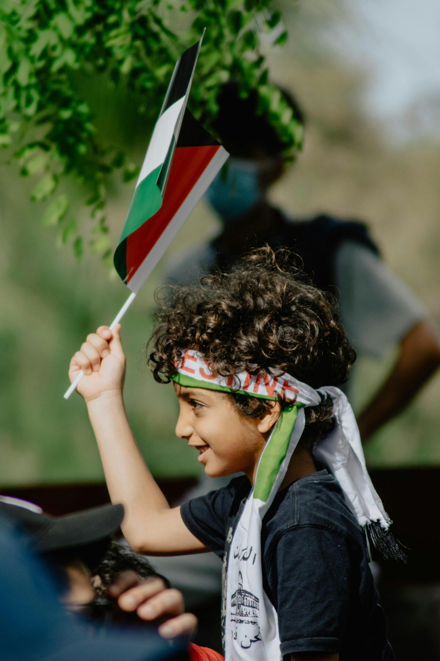 Boy in blue and white shirt holding a Palestinian flag