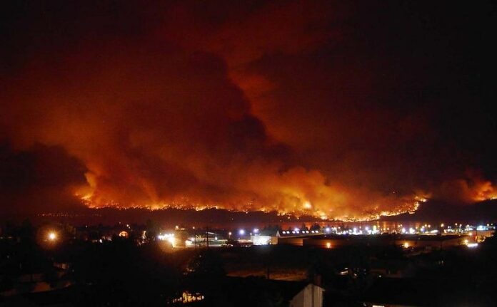 A large orange fire covering the sky above a town.
