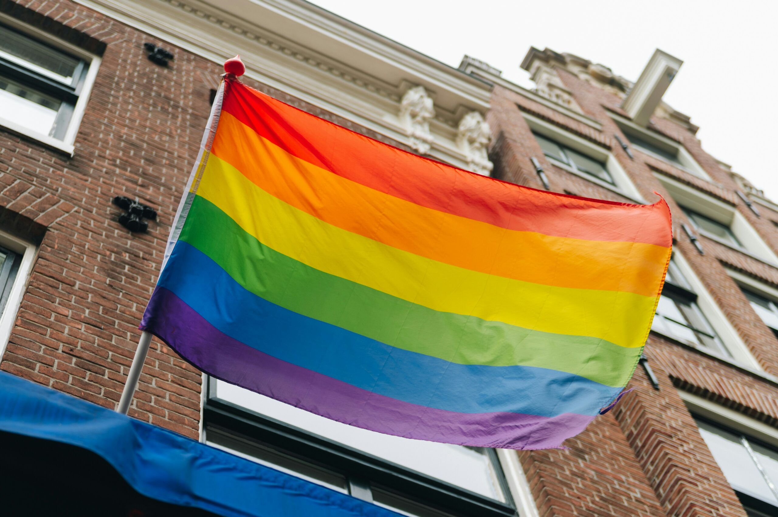 a rainbow pride flag hanging off a brick building