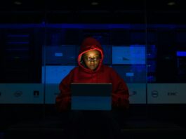 Person wearing a red hoodie sitting in the dark in front of a tablet.