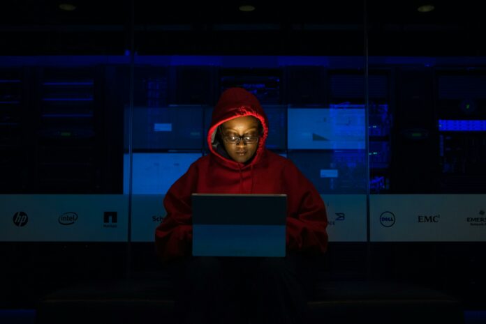 Person wearing a red hoodie sitting in the dark in front of a tablet.