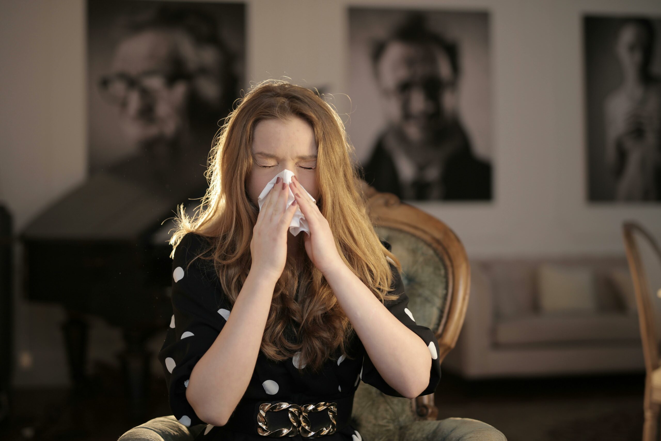 Woman wearing a black and white polka dot dress sneezing into a tissue.