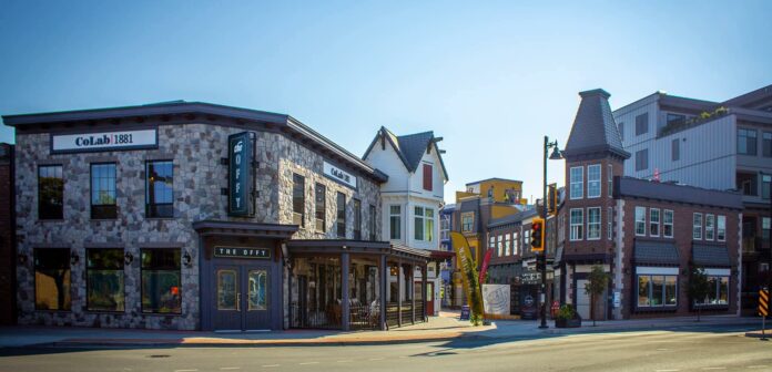 Brick and cobblestone buildings line an alleyway adorned with restaurant patios and small stores. Through the alley, more colourful buildings can be seen.