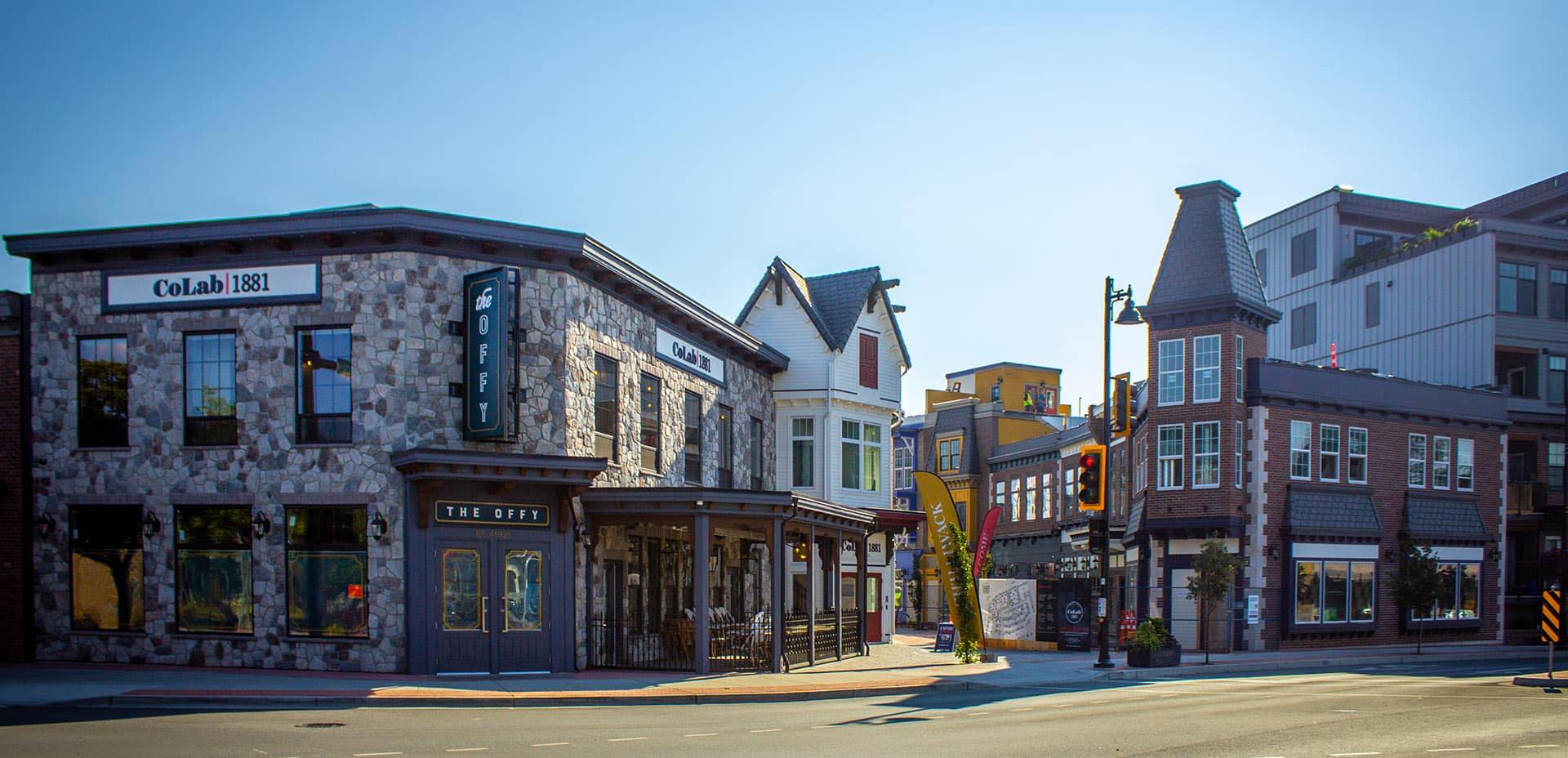 Brick and cobblestone buildings line an alleyway adorned with restaurant patios and small stores. Through the alley, more colourful buildings can be seen.