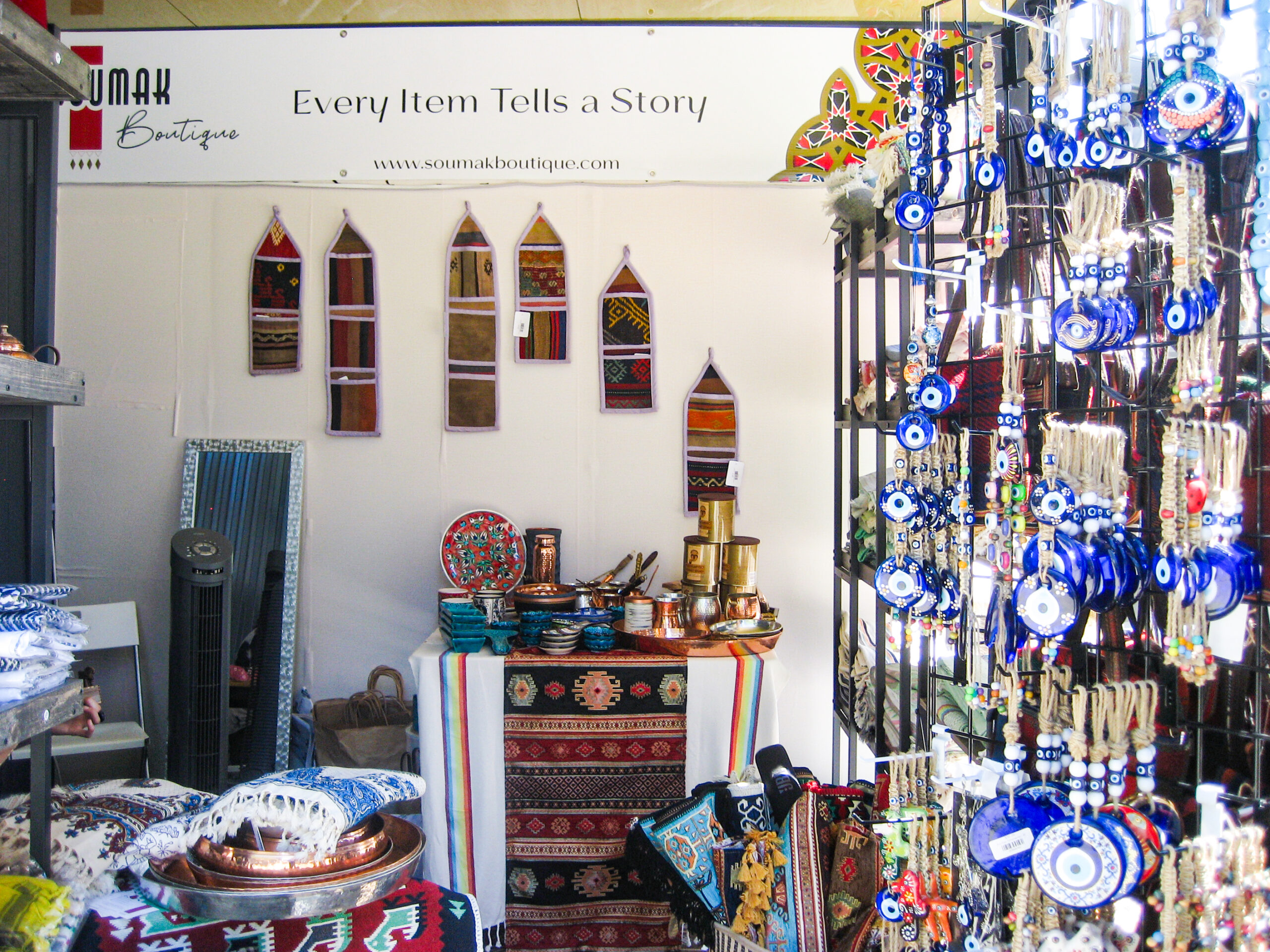 A small storefront adorned with copper dishware, ornately woven rugs, and charms with a blue eye. A banner at the top says “every item tells a story.”