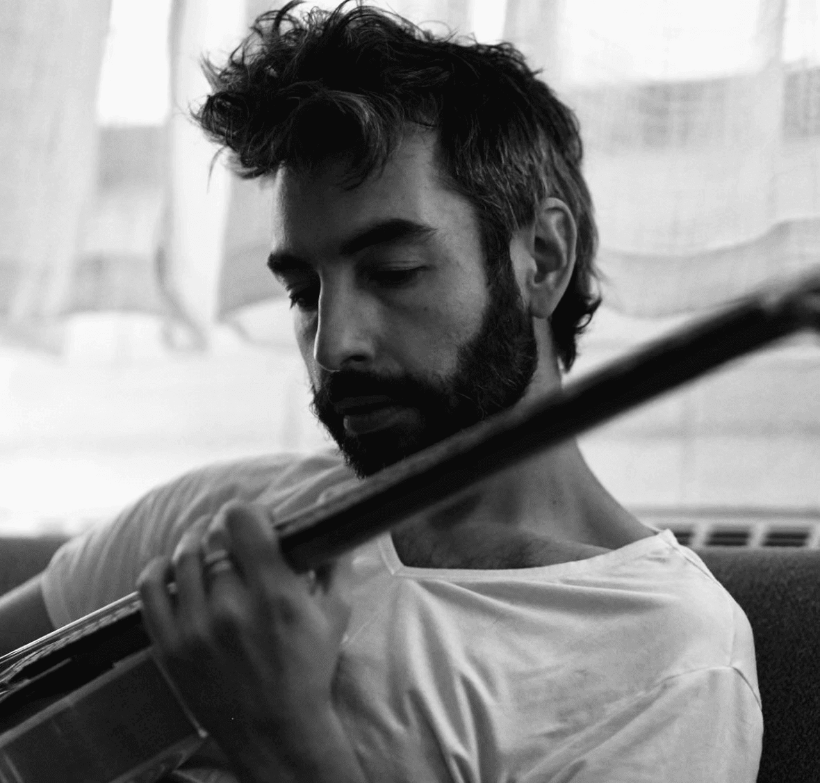 A black and white close-up of a man holding a guitar and playing it, his facial features relaxed.