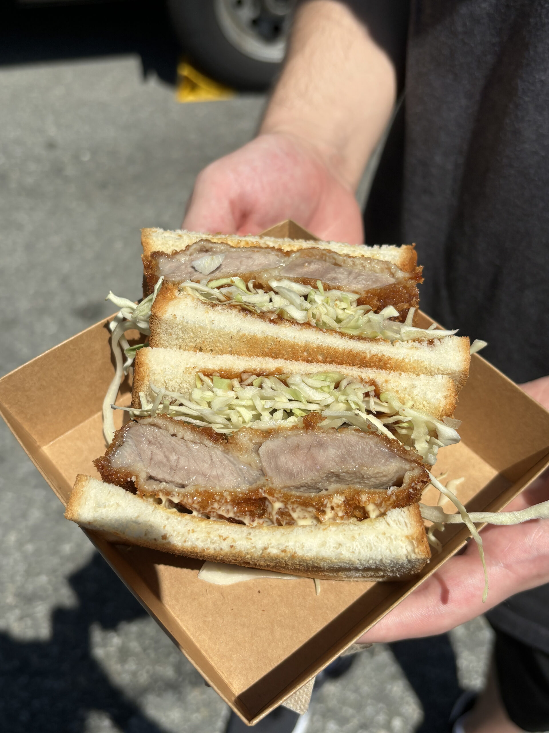 A sandwich with toasted white bread stuffed with sliced white cabbage and golden-brown fried pork cutlets.