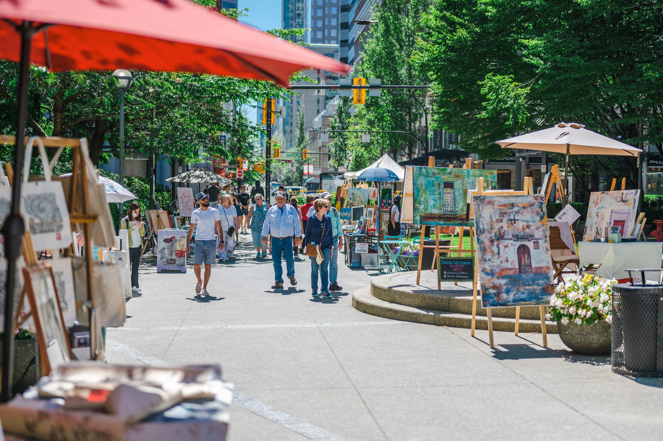 Colourful paintings on easels displayed along a busy street in downtown Vancouver.