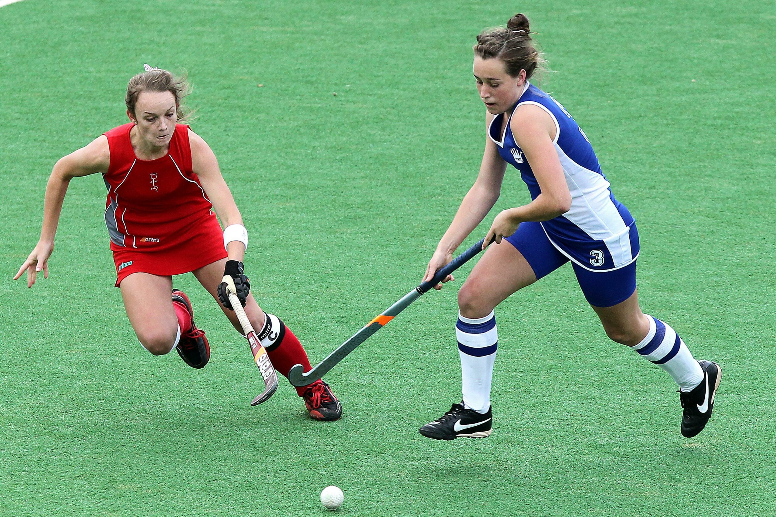 Two women competing for a goal in field hockey.