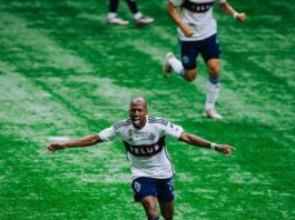 A player wearing blue and white runs down a grassy field with his arms outstretched like a flying bird.