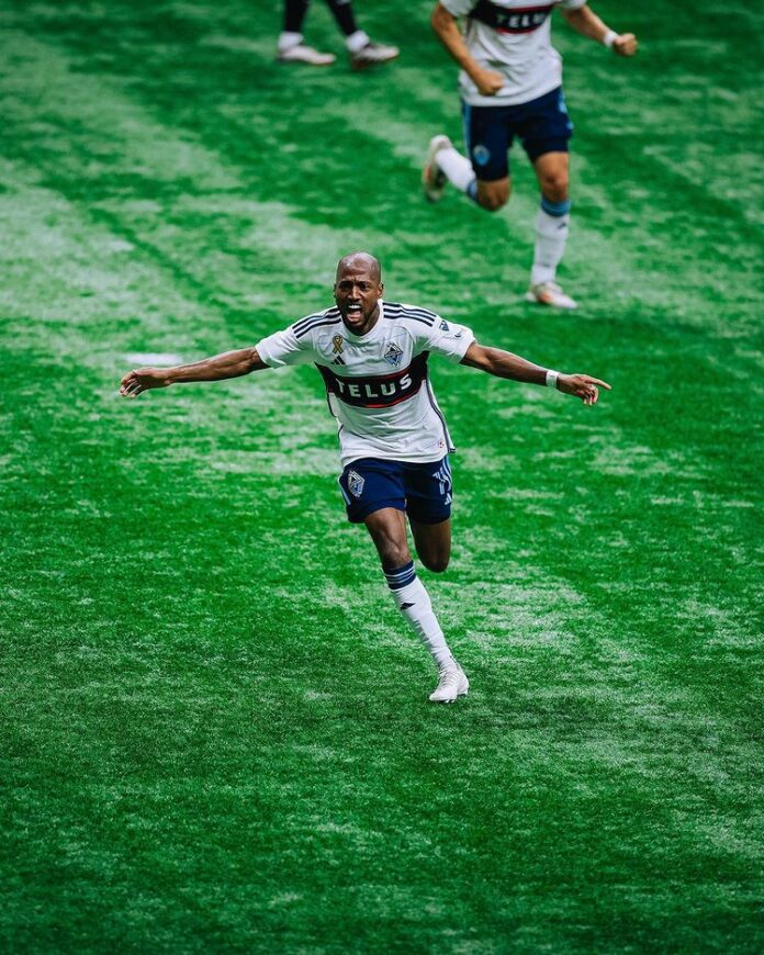A player wearing blue and white runs down a grassy field with his arms outstretched like a flying bird.
