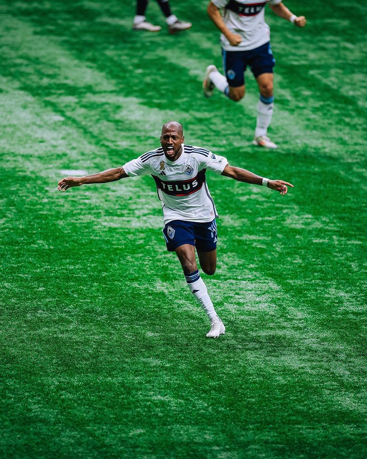 A player wearing blue and white runs down a grassy field with his arms outstretched like a flying bird.