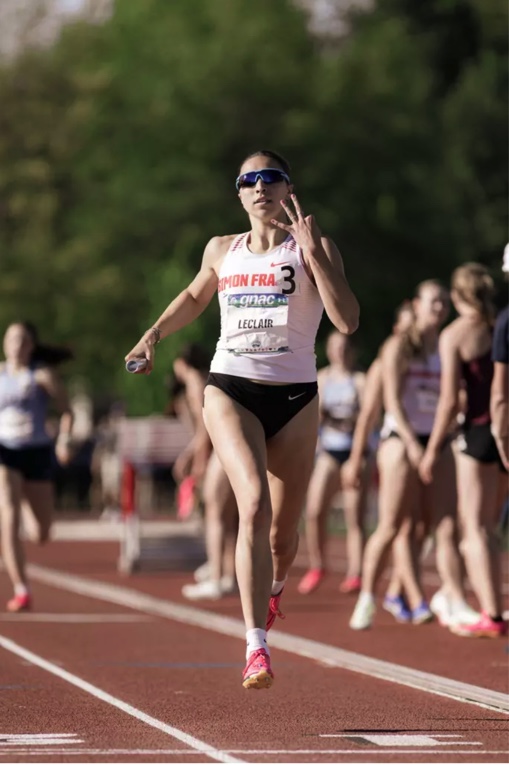 Sprinter Marie-Éloïse Leclair holdng up three fingers while running with a baton in her hand.