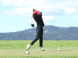 A girl with a red baseball cap, black pants, and a black long sleeve swings a driver.