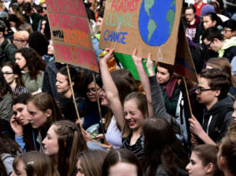 This is a photo of a bunch of young climate activists, with one activist laughing as she holds up a sign