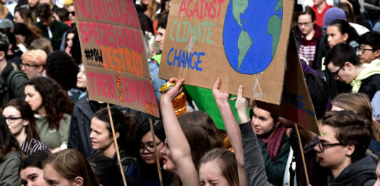 This is a photo of a bunch of young climate activists, with one activist laughing as she holds up a sign