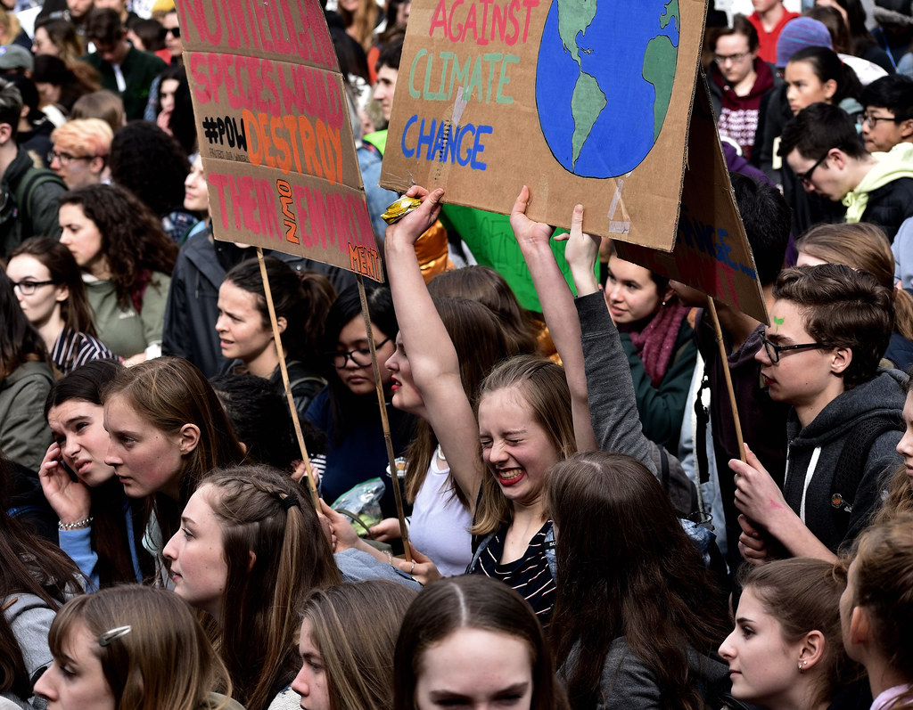 This is a photo of a bunch of young climate activists, with one activist laughing as she holds up a sign