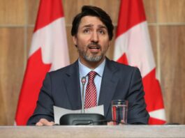 This is a photo of Justin Trudeau speaking in front of two Canada flags in a medium shot