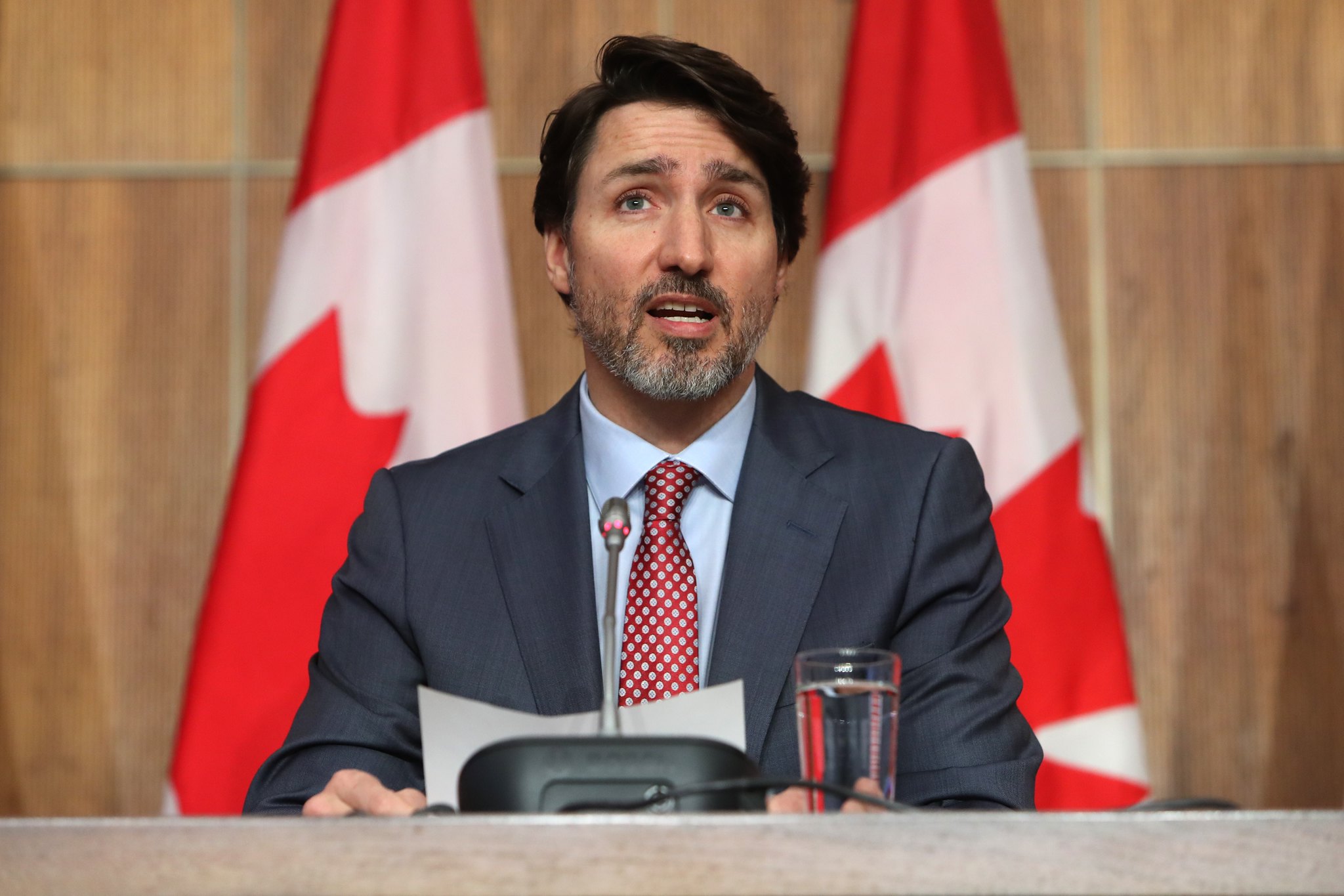 This is a photo of Justin Trudeau speaking in front of two Canada flags in a medium shot