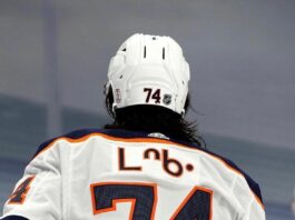 A hockey player skating away from the camera with his name plate written in Cree syllabics.