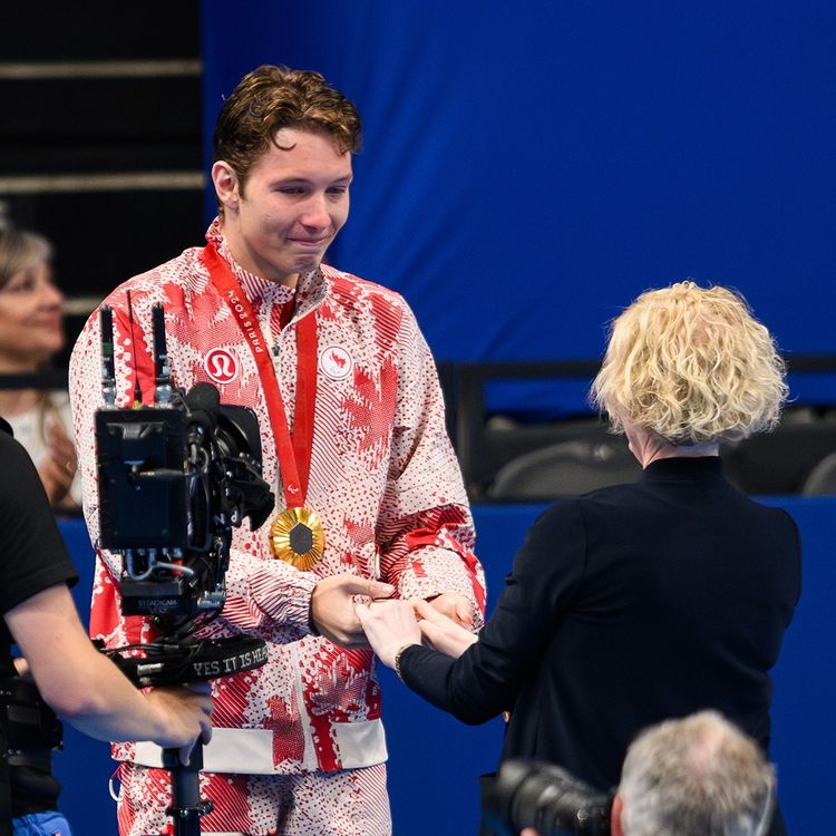 A man in a Canadian uniform tearfully shakes hands with a woman. Hanging from his shoulders is a gold medal.