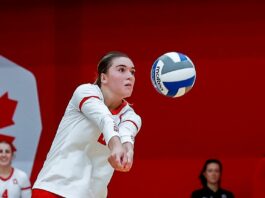 A woman in red and white attempts to bump a volleyball.