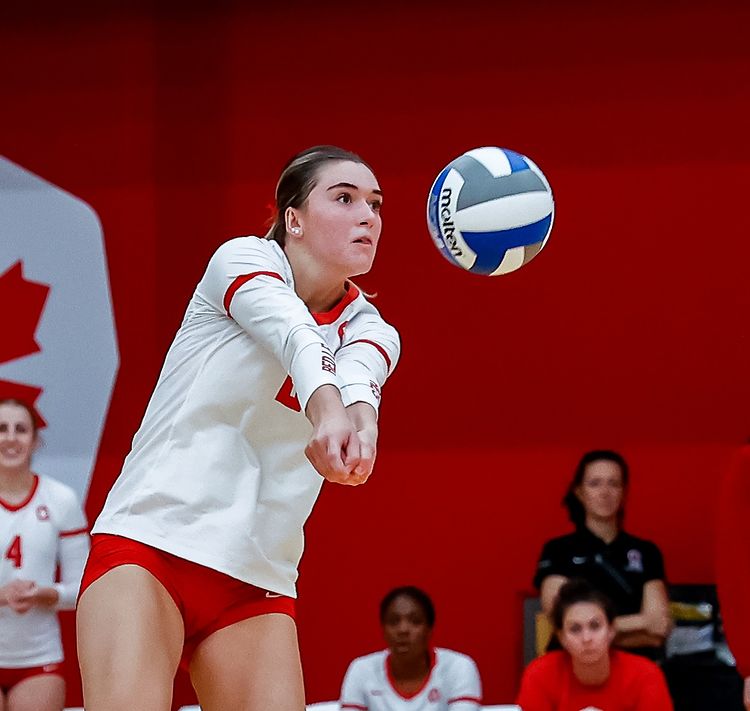 A woman in red and white attempts to bump a volleyball.