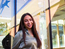 This is a photo of Vanessa Hum in front of a Feather Friendly dots window solution. It says, “LET’S MAKE SFU BIRD SAFE.”