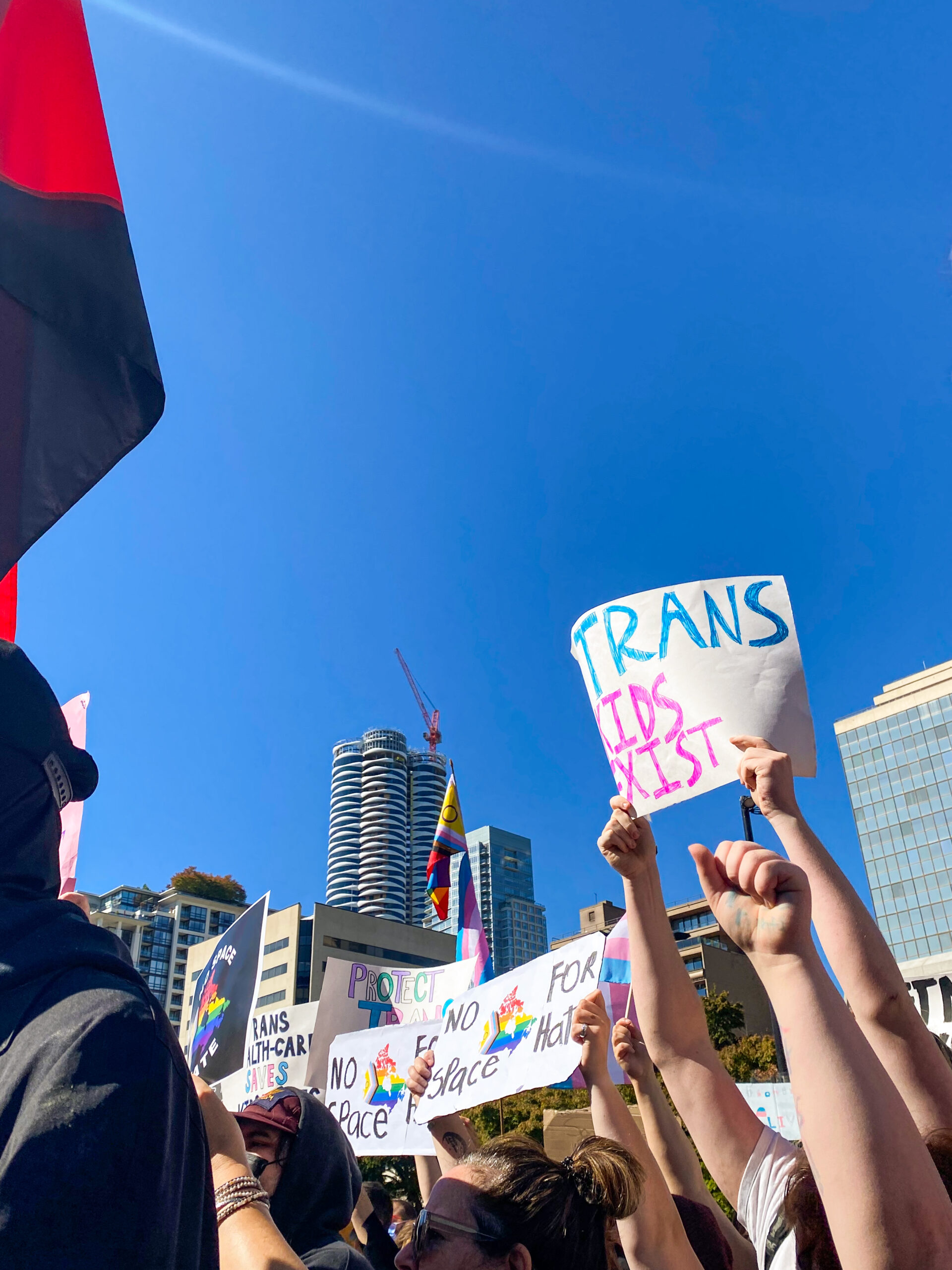 This is a photo of multiple pro-SOGI posters at a counter-protest in Vancouver. One reads, “TRANS KIDS EXIST.”