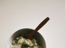 A bowl of creamy white tzatziki dusted in sprouts and green specks.