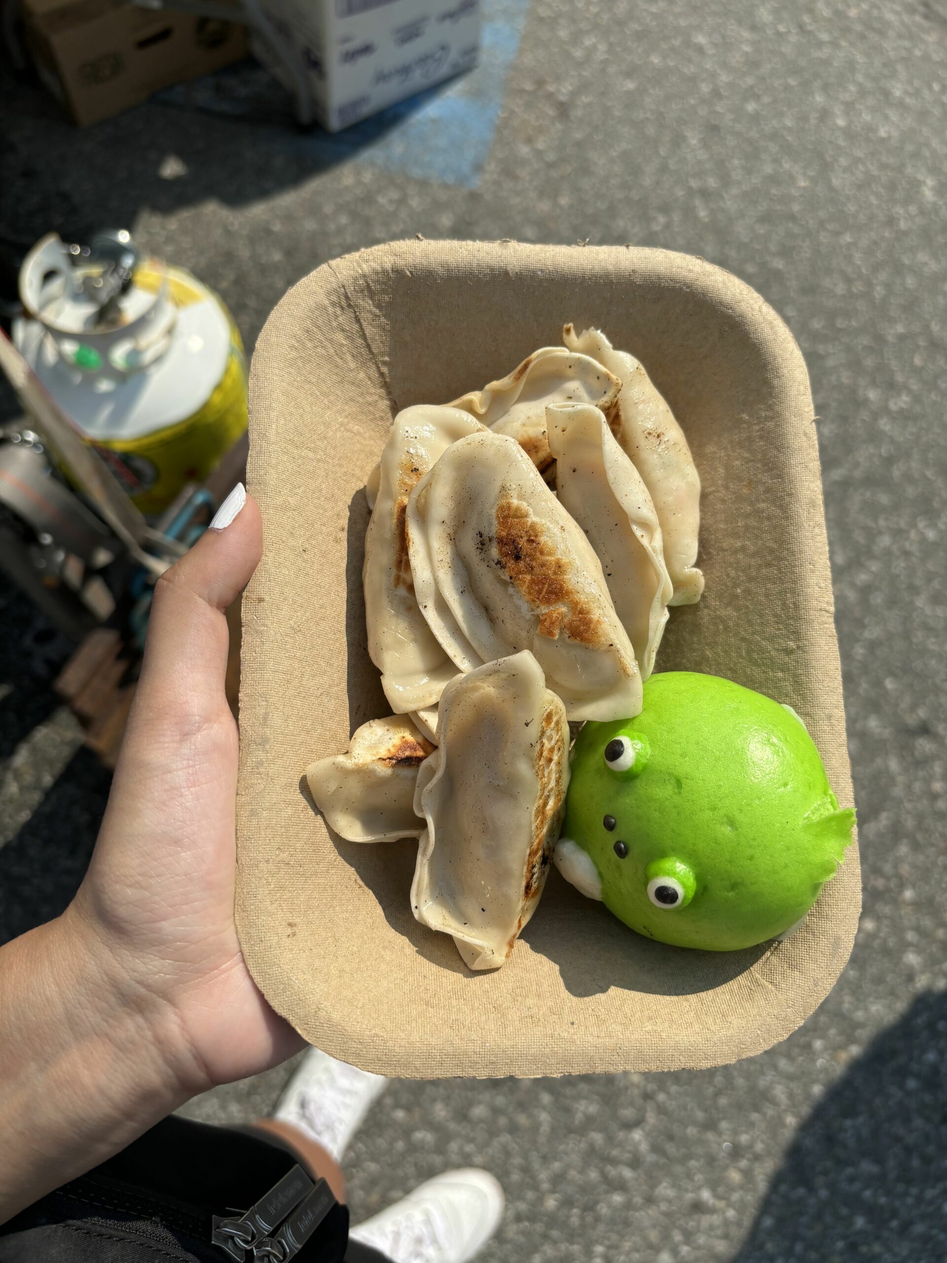 A container filled with pan-fried dumplings and a green frog bun.