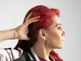 This is a photo of a woman with red hair moving her hair back to show her hearing aid.