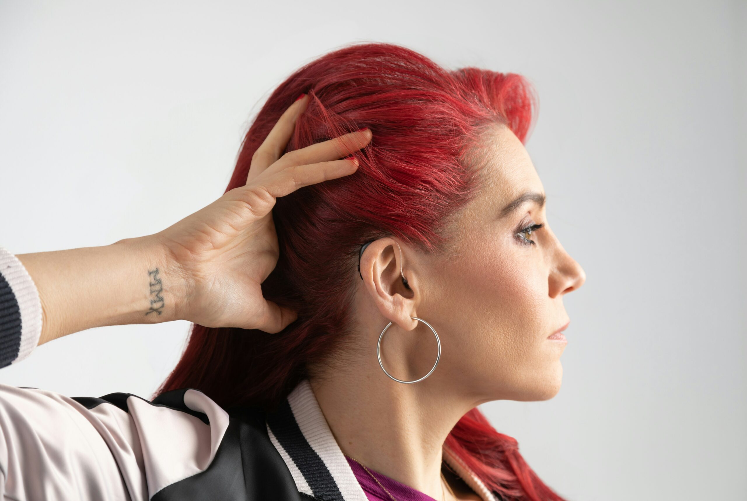 This is a photo of a woman with red hair moving her hair back to show her hearing aid.