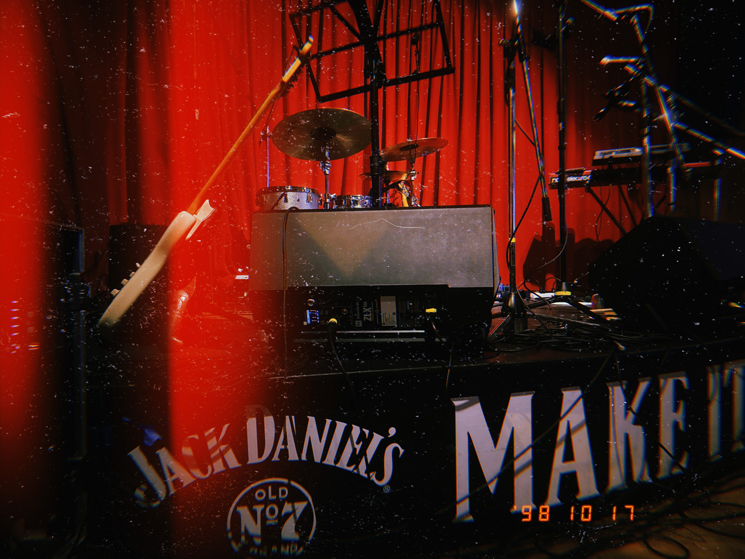 a grainy filter over a stage hosting a guitar, a drumset, and a microphone stand. In the background is a scarlet curtain.