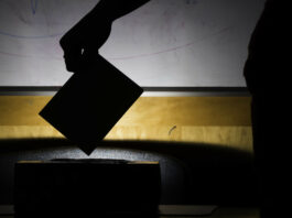 A silhouette of ballot box against a dark background, with a hand putting a ballot in