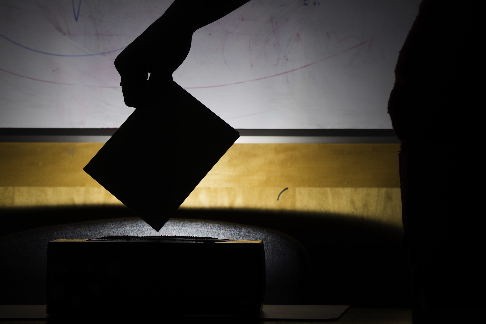 A silhouette of ballot box against a dark background, with a hand putting a ballot in