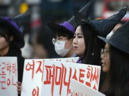 This is a photo of three people in witch hats holding up signs in Korean as part of the 4B movement.