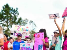 A bunch of girls stand holding pink and purple signs reading praise for Caitlin Clark and women’s sports, including “little girls, big dreams” and “we love Caitlin.”