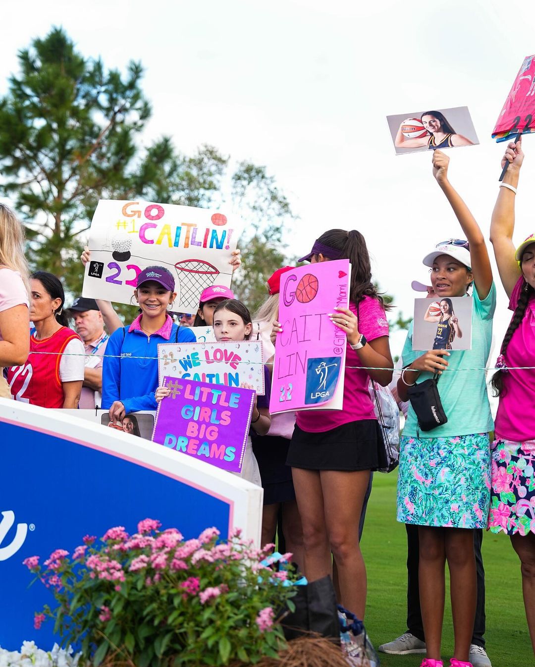 A bunch of girls stand holding pink and purple signs reading praise for Caitlin Clark and women’s sports, including “little girls, big dreams” and “we love Caitlin.”