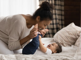 This is a photo of a mother smiling down at her baby on a bed.