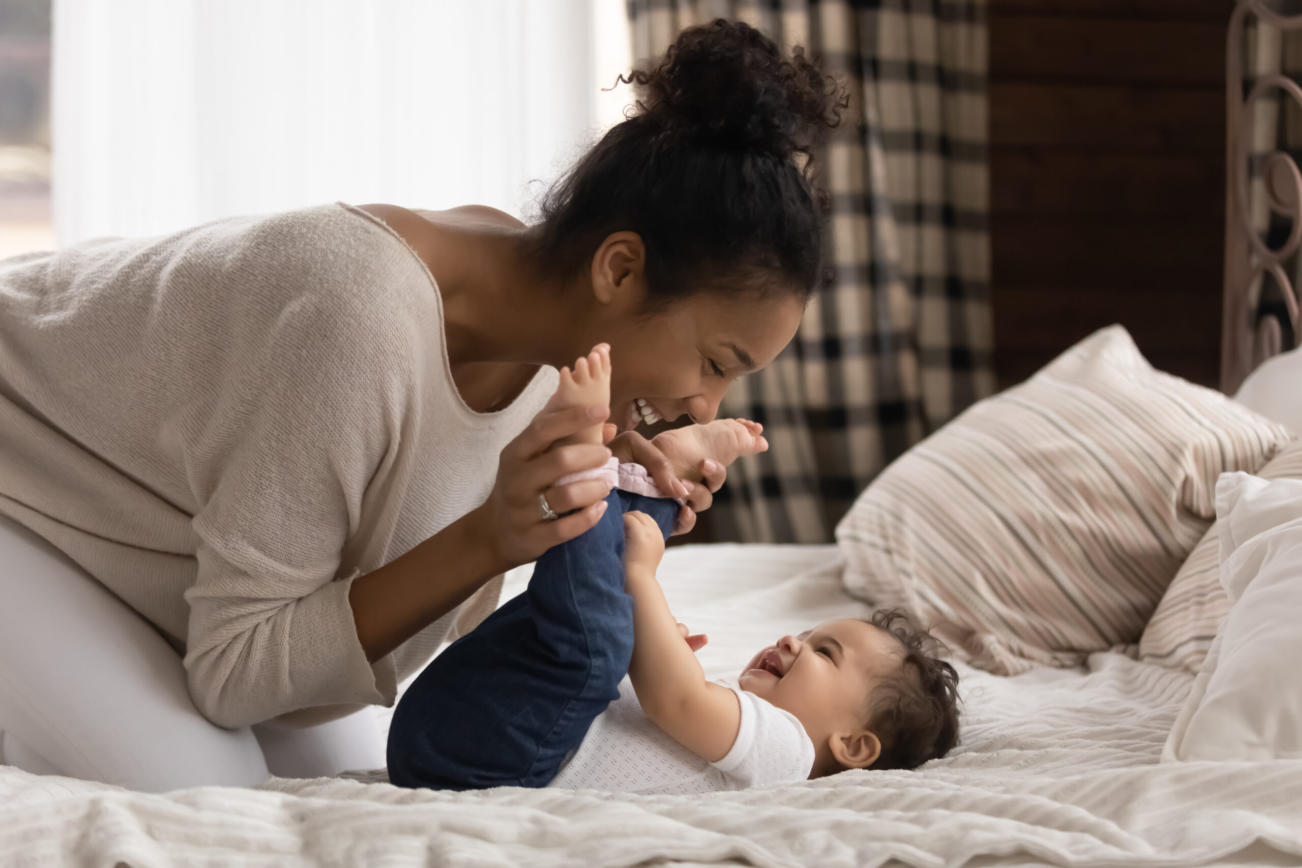 This is a photo of a mother smiling down at her baby on a bed.