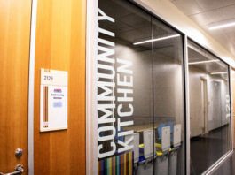 A glass window with the words “community kitchen” printed sideways. A wooden door with the number 2125 on a board sits beside it.