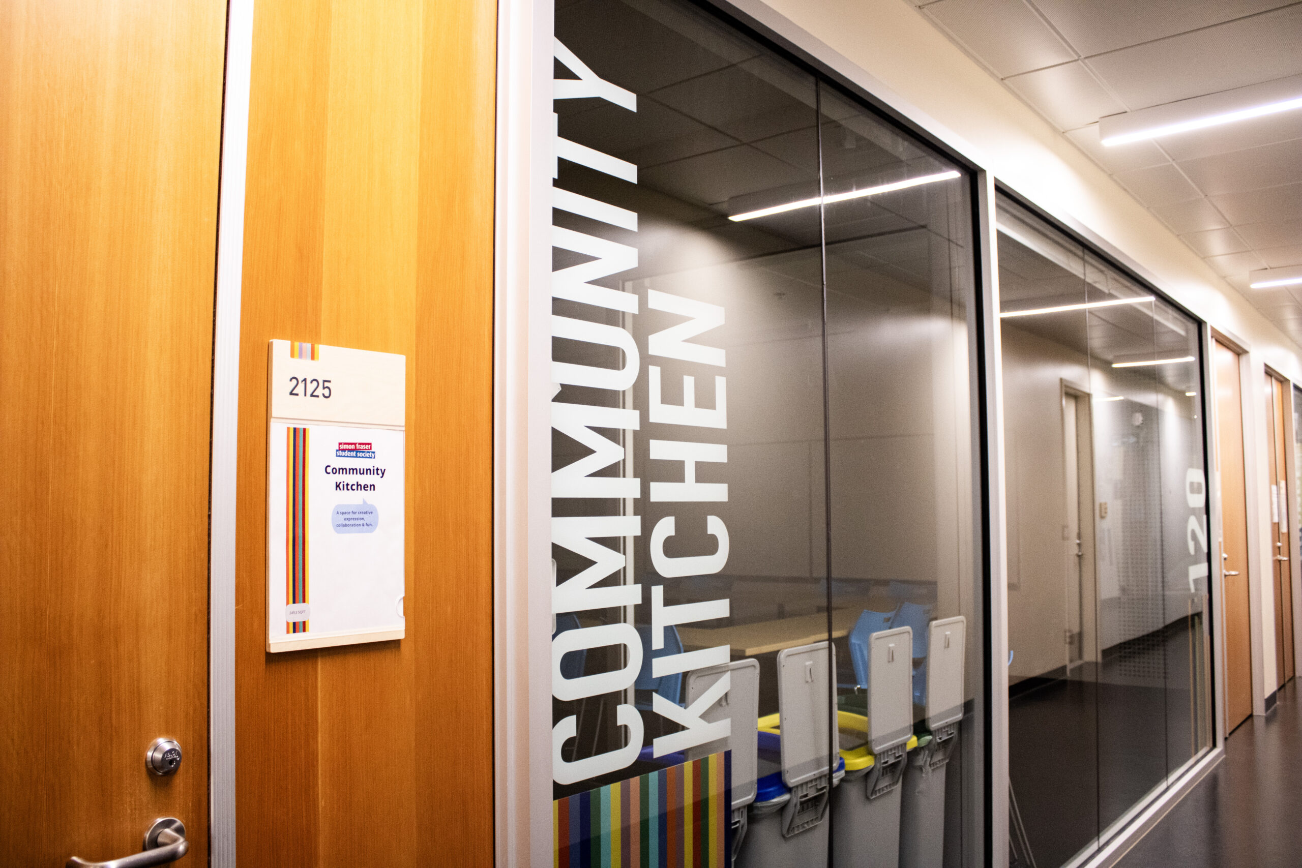 A glass window with the words “community kitchen” printed sideways. A wooden door with the number 2125 on a board sits beside it.