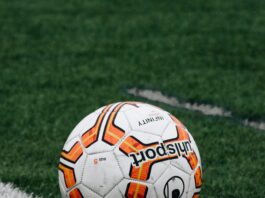 A white soccer ball lined with orange pentagon patterns sits on a green grass field.