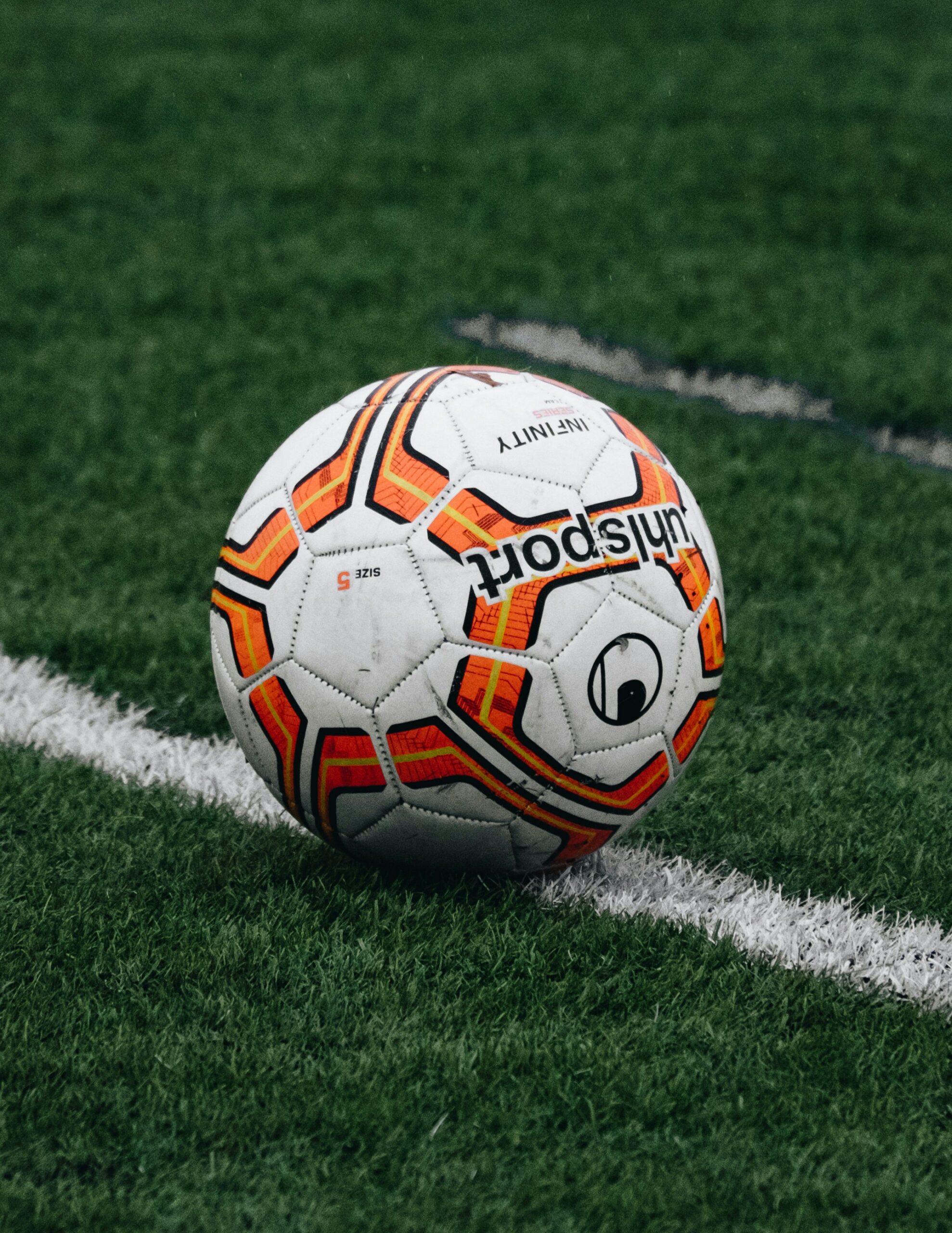 A white soccer ball lined with orange pentagon patterns sits on a green grass field.