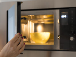 A hand closing a microwave with a bowl inside